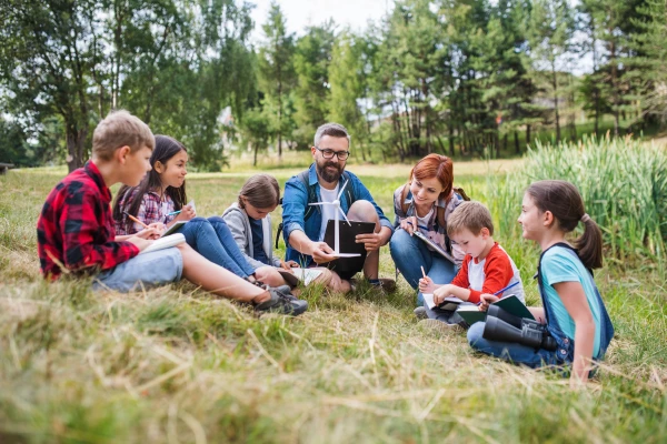 Kinder sitzen im Gras und folgen den Ausführungen eines Lehrers, der ein Modell eines Windrades hält
